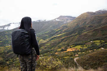 Hermosa foto de una feliz viajera hispana con una mochila en la cima de montañas verdes