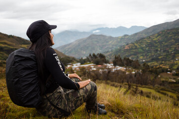 Hermosa foto de una feliz viajera hispana con una mochila sentada en la cima de montañas verdes