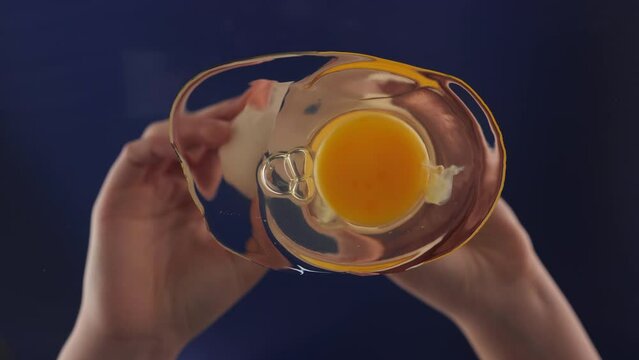 Breaking and spilling egg onto glass surface. Bottom up view. Female hands holding a cracked egg. Breaking an egg seen from the frying pan. Slow motion. Camera pointing up.