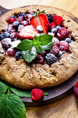 Whole-grain galette with plums and berries on dark background, top view