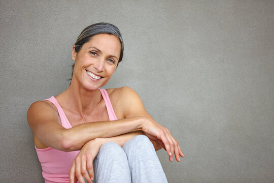 Living a healthy lifestyle. Portrait of an attractive mature woman in gymwear sitting against a gray wall.