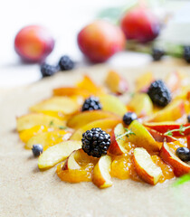 Preparation of whole-grain galette with plums, blackberries and blueberries on white table, top view