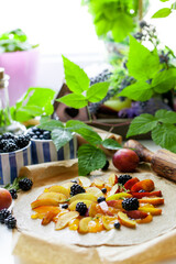 Preparation of whole-grain galette with plums, blackberries and blueberries on white table, top view