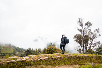Fototapeta premium Vista trasera de una mujer con una mochila en una caminata. Mujer joven de pie en un camino disfrutando de la vista panorámica desde la parte superior.