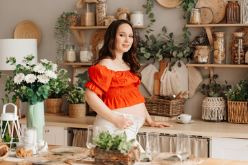 a beautiful pregnant woman in a romantic orange blouse and trousers in kitchen. 