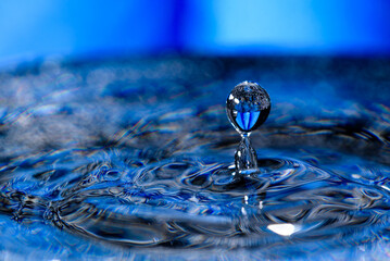 Macro shot shallow focus shot of a drop falling on detal blue wavy water - obrazy, fototapety, plakaty