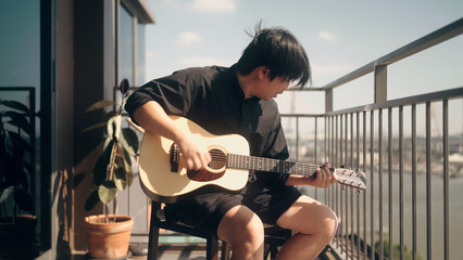 man relaxing by playing guitar on the balcony of the condo - obrazy, fototapety, plakaty