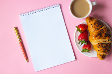 Pink note with pencil and sharpener, coffee cup, croissant with strawberries on pink background