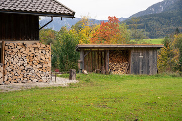 Split and stacked firewood stored in wooden shed in countryside with trees and hills in background