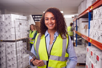Portrait Of Female Worker Inside Busy Warehouse Checking Stock On Shelves Using Digital Tablet 