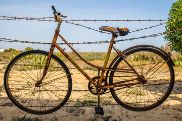 Fototapeta na wymiar Old rusty bicycle hanging on barbed wire in Farol Island, Portugal