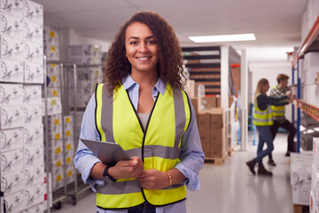 Portrait Of Female Worker Inside Busy Warehouse Checking Stock On Shelves Using Digital Tablet 