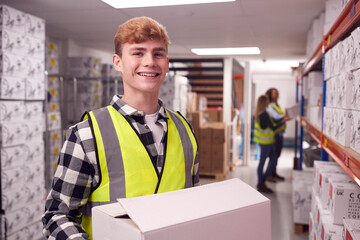 Portrait Of Male Worker Inside Busy Warehouse Carrying Box