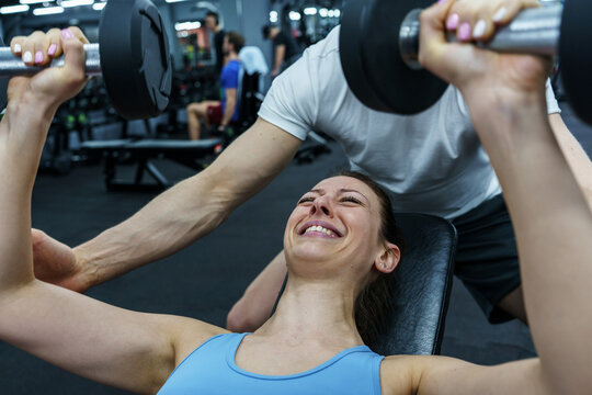 A couple exercising together at the gym. Female try to lift heavy dumbbells ,pushing to the limit.	
