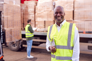 Portrait Of Male Freight Haulage Manager Standing By Truck Being Loaded By Fork Lift 