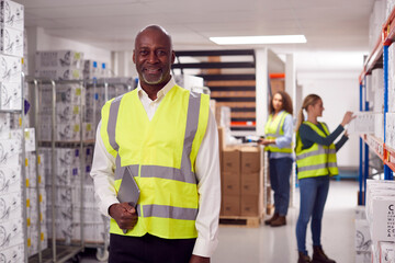 Portrait Of Team Leader With Digital Tablet In Warehouse With Staff Picking Items From Shelves 