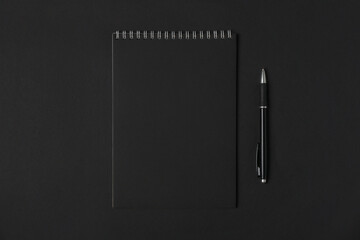 Blank notebook with blank black sheets and pen on dark background, copy space, top view. Business or education concept.