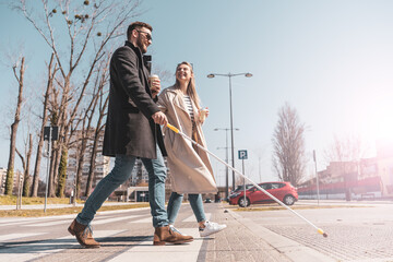 A blind male person using a white cane and walks with his female friend.They walk down the...
