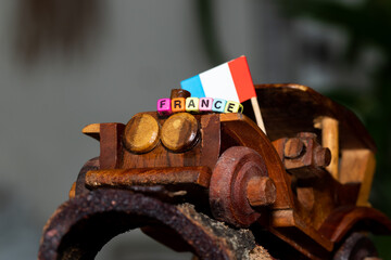 Mote alphabet blocks arranged into "France" on a miniature wooden car with the national flag in the background.