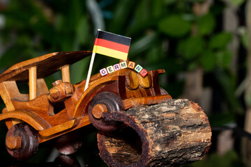 Mote alphabet blocks arranged into "Germany" on a miniature wooden car on the background of the national flag.