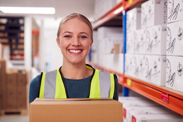 Portrait Of Female Worker Holding Box Inside Warehouse 