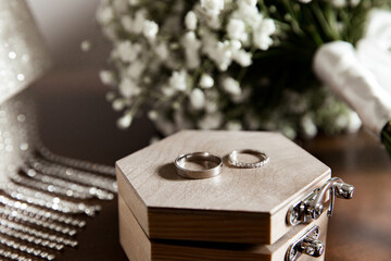 Wedding rings lie on a wooden box next to the bride's bouquet