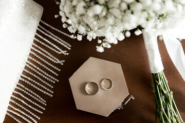Wedding rings lie on a wooden box next to the bride's bouquet