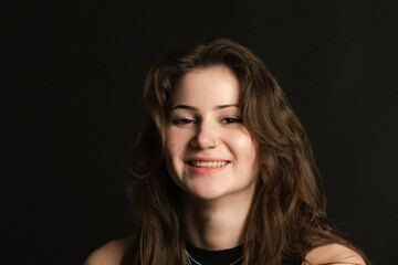 The young lady in black smiles. Black background. Caucasian. Brunette. Piercing. copy space