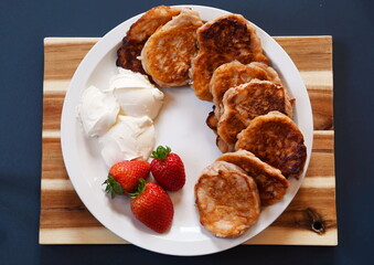 Strawberry fritters with sour cream on a white plate and a board for breakfast,