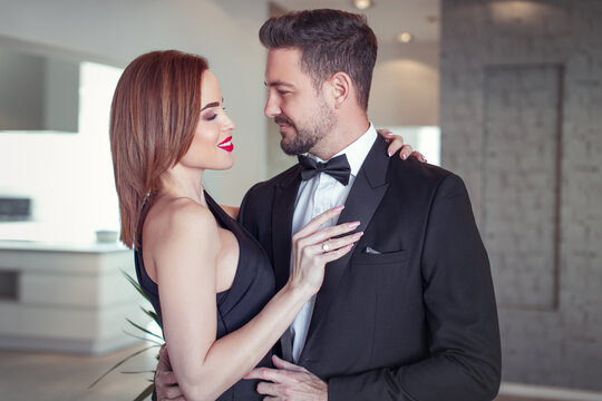 Happy rich woman holding sexy boyfriend in tuxedo