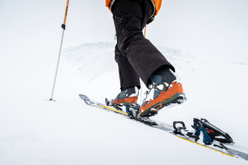 Close-up of the legs. Winter skitour freeride in cloudy weather, snow-capped mountains against the backdrop of a glacier. Skier man in full gear climbs uphill in a skitour