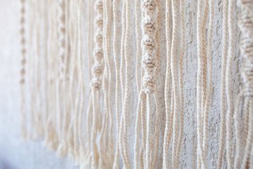 Handmade macrame wallhanging. 100% cotton wall decoration with wooden stick hanging on a white wall.   Macrame braiding and cotton threads. Female hobby.  ECO friendly modern concept in the interior