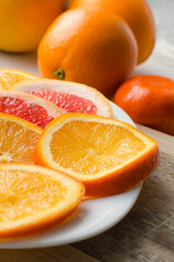 Slices, whole citruses, Tangerines, oranges, grapefruits are lying on a plate. Summer exotic tropical fruits. Vertical photography.