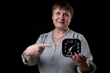 An elderly woman holds an alarm clock in her hand.