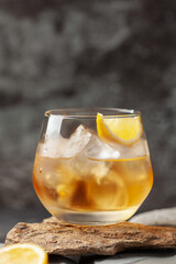 Glass of whiskey with lemon and ice on stone background.