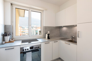 Small modern white kitchen with oven, sink, coffee maker and stove with large bright window with a view