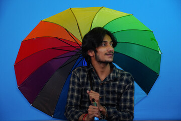 Young handsome man holding colorful umbrella and giving amazed expression, fear and excited face.