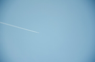 A passenger plane flies across the blue sky and leaves a white path.