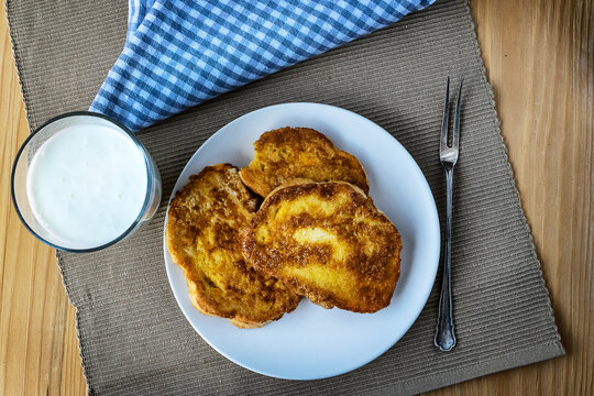 French toast - Przenice - slices of bread soaked in beaten eggs and milk and fried, with a glas of yogurt on a wooden table. Eggy bread, Bombay toast, German toast, gypsy toast or poor knightsles