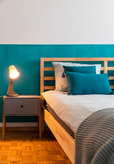 Detail of wooden bed with turquoise wall and many pillows on the sheets