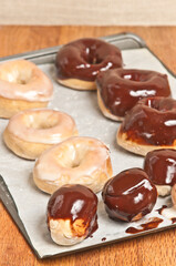 top view, medium distance of a group of freshly baked donuts, coated with vanilla or chocolate frosting , cooling on parchment paper and metal baking tray
