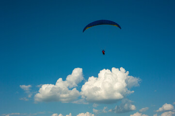 Blue paraglider flying in the blue sky against the background of clouds. Paragliding in the sky on...