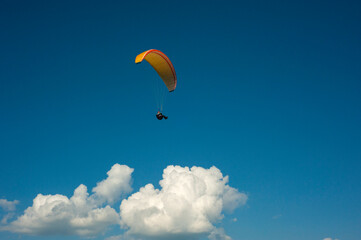 Yellow paraglider flying in the blue sky against the background of clouds. Paragliding in the sky on a sunny day.