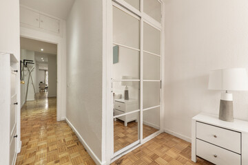 Fototapeta na wymiar Bedroom with white fitted wardrobe with mirrored sliding doors, long hallway with oak floorboards and white painted walls
