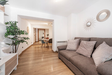 room with a three-seater sofa connected to a dining room with a wooden table that gives access to other rooms