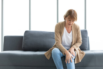 senior woman suffering from knee ache on sofa - obrazy, fototapety, plakaty