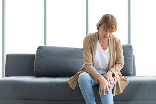 Senior Woman Suffering From Knee Ache On Sofa