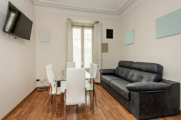 Fototapeta na wymiar Living room with a three-seater black leather sofa and a glass dining table with white leather chairs and a flat-screen TV on the wall