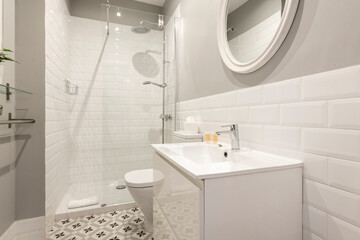 Bathroom with one piece sink, white framed round mirror and white tiled shower stall with glass partition