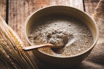 cuchara de madera en un bol con harina integral de trigo y espigas de trigo sobre una mesa de madera rústica
